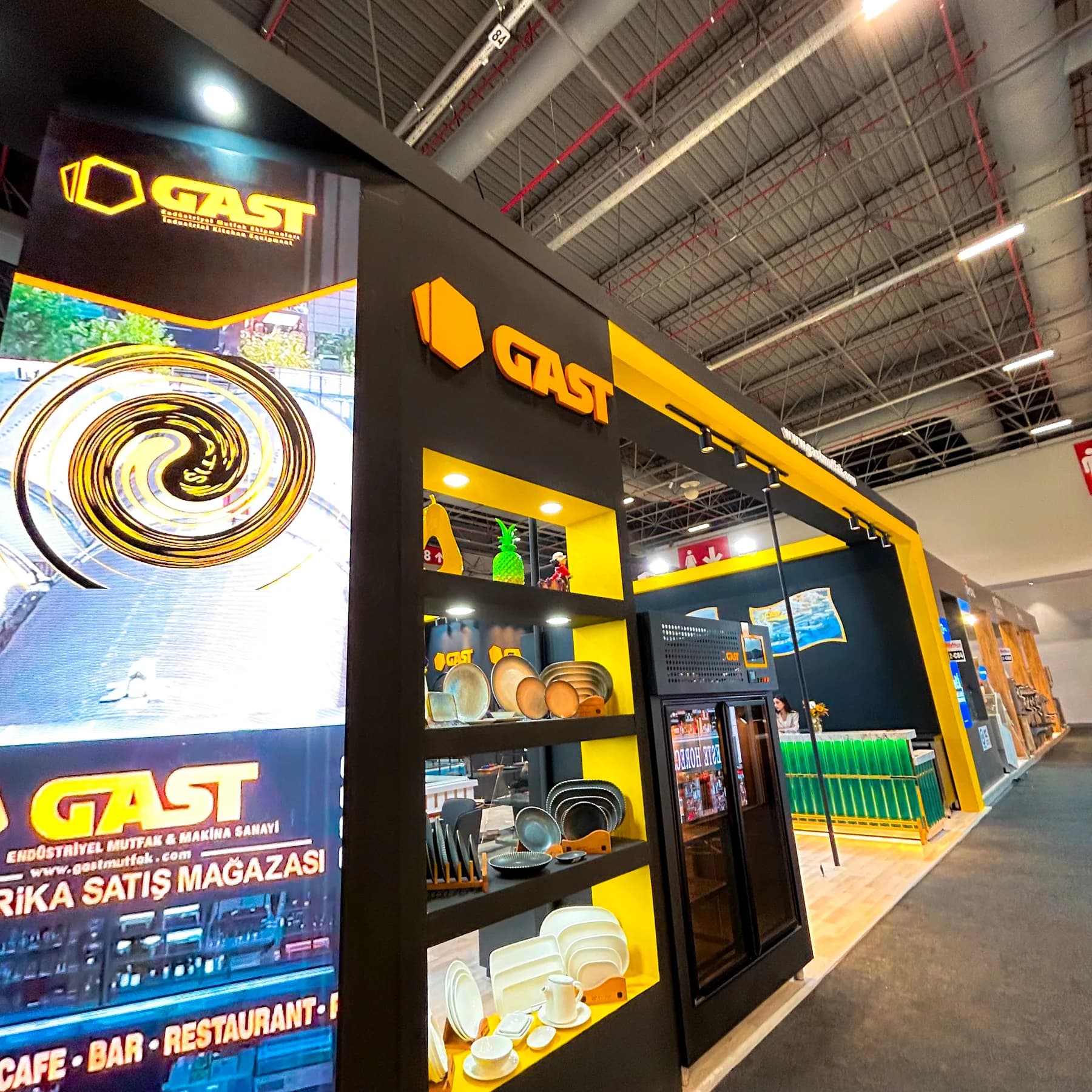 Gast — Mutfak ekipmanı sunumları için siyah ve sarı stand mimarisi.